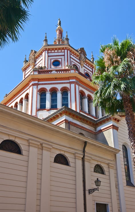 Chiesa di Santo Stefano in Rapallo, Italy — close-up of the church’s striking octagonal dome with red and white detailing, arched windows, and statues, framed by palm trees under a bright blue sky..