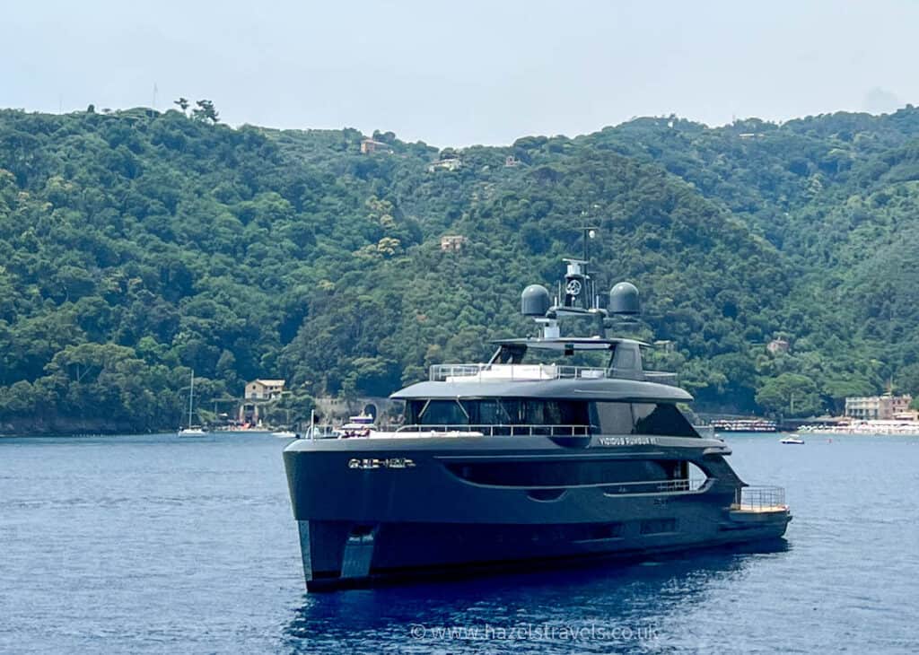 A large yacht is anchored in calm blue waters near a lush, green hillside, offering a serene backdrop for those exploring things to do in Portofino.