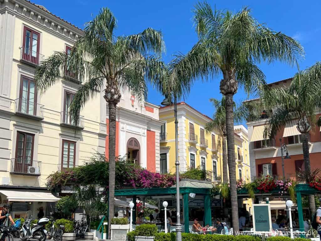 Piazzo Tasso, the town square in Sorrento with palm trees and coloured buildings. This square contains lots of things to do in Sorrento.