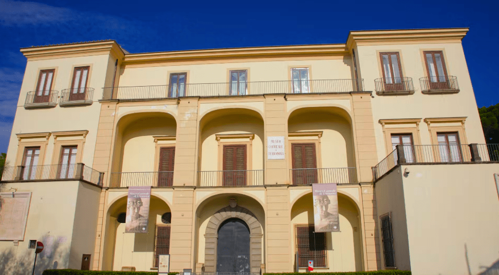 A large, beige three-story building in Sorrento boasts arched entrances and charming balconies set against a clear blue sky.