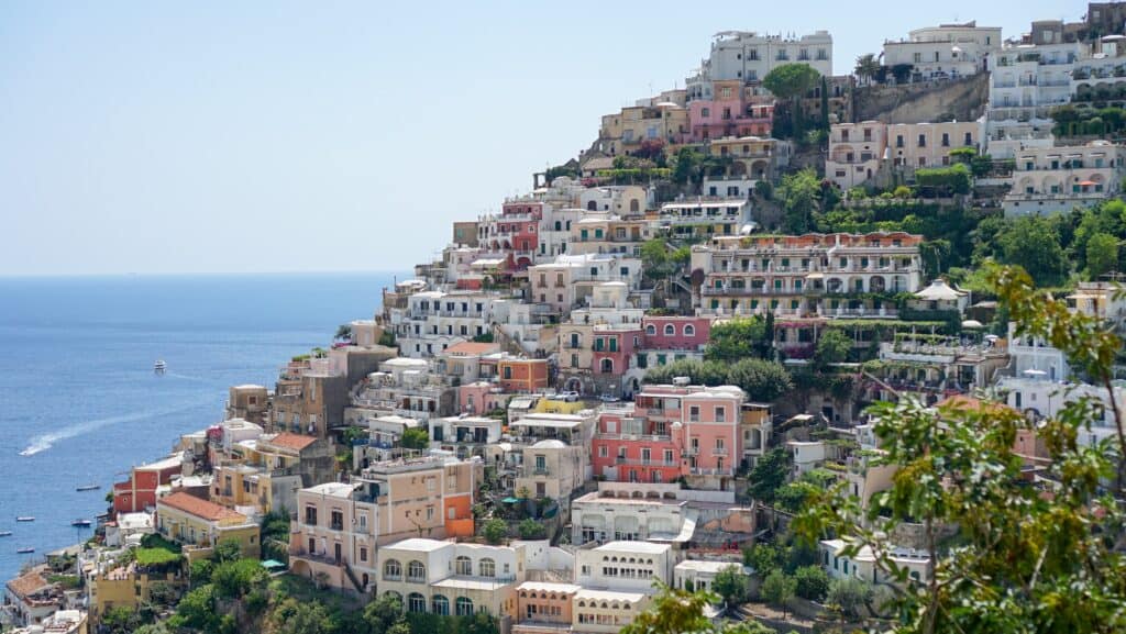 Colorful cliffside buildings and lush greenery define the picturesque town of Positano, with the sparkling sea in the background and boats elegantly bobbing in the water.