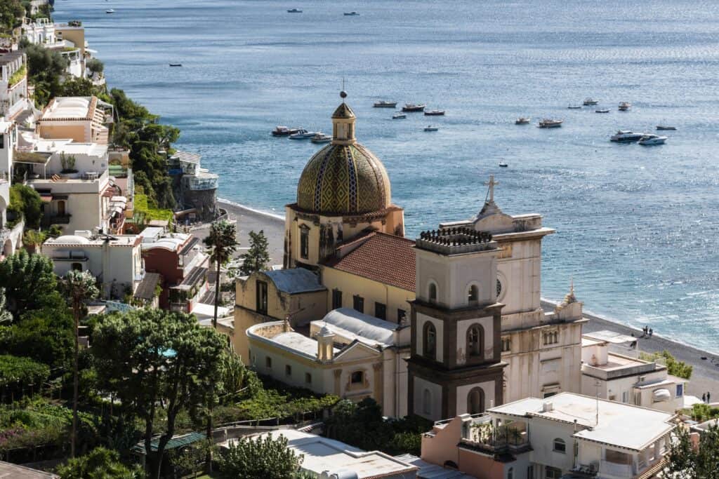 Perched along the azure Amalfi Coast, Positano is a coastal town renowned for its domed church, vibrant buildings cascading down cliffs, and charming boats gently swaying on the glistening sea.