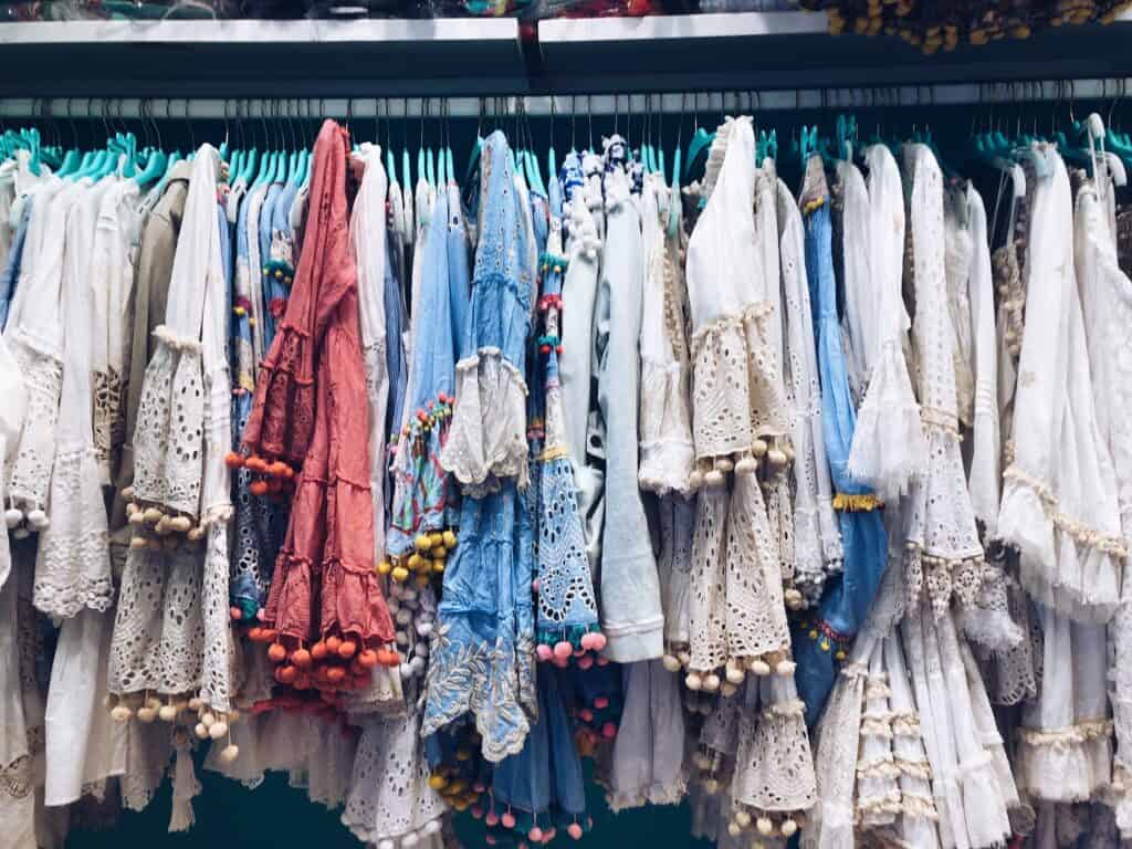A variety of colorful, lace-trimmed dresses with pom-pom embellishments hang on a rack, echoing the vibrant charm of things to do in Positano.