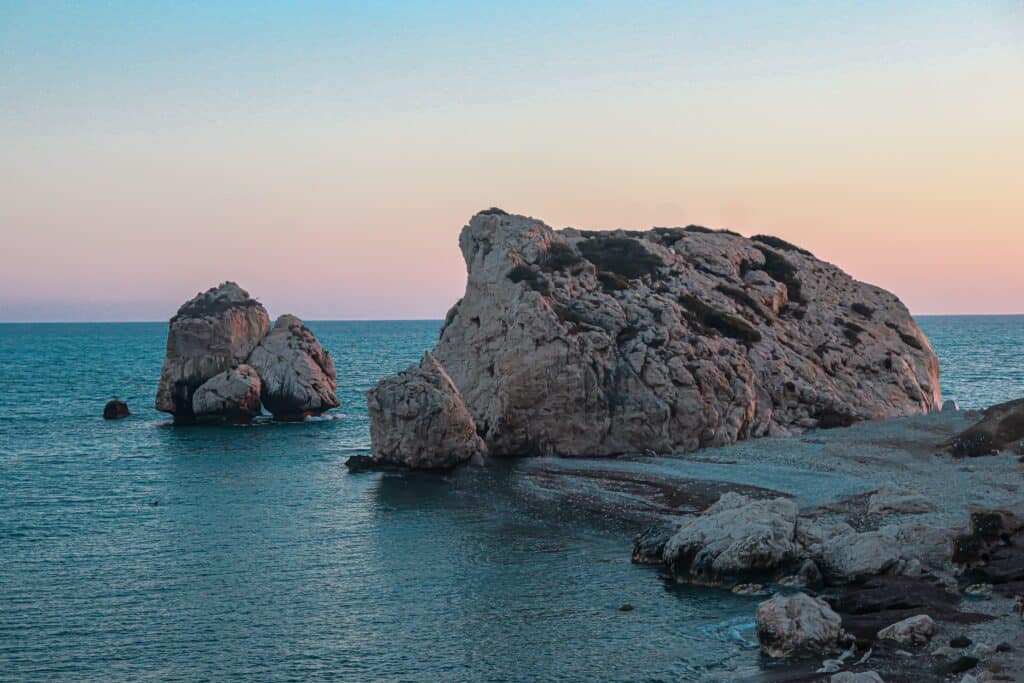 Two large rocky formations rise from the sea near the shore at sunset.