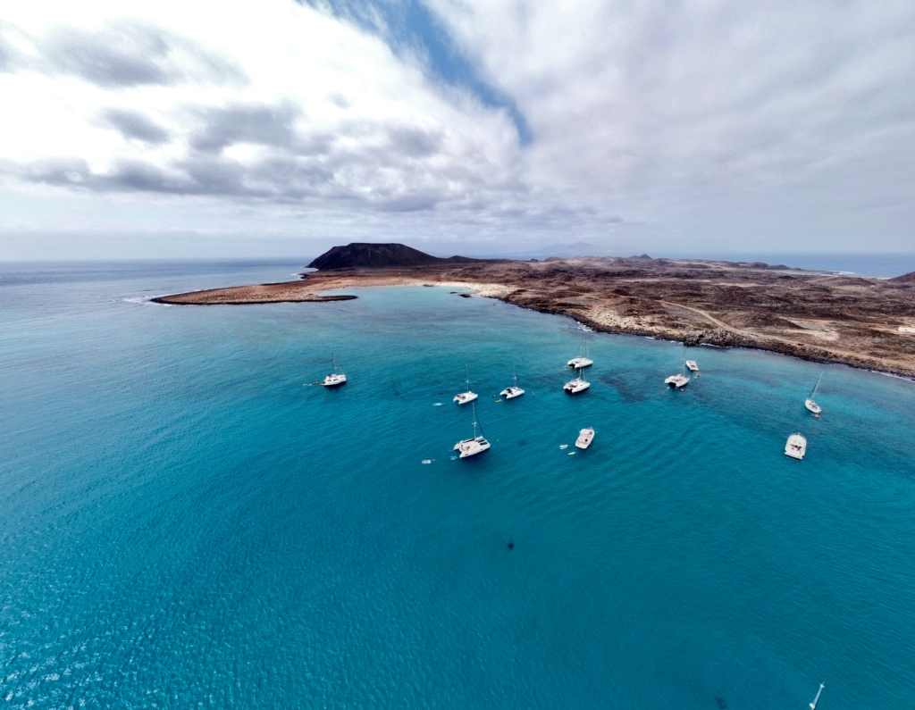 View of a small Island, brown volcanic landmass, turquoise bloue sea and small white boats and catamarans.