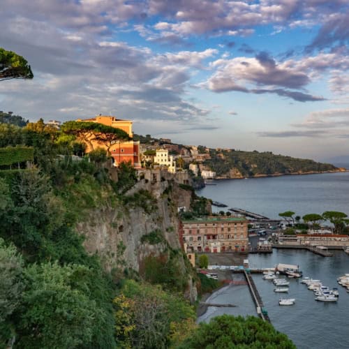 Landscape view of Sorrento harbour with green cliffs and trees on the left and boats on the right