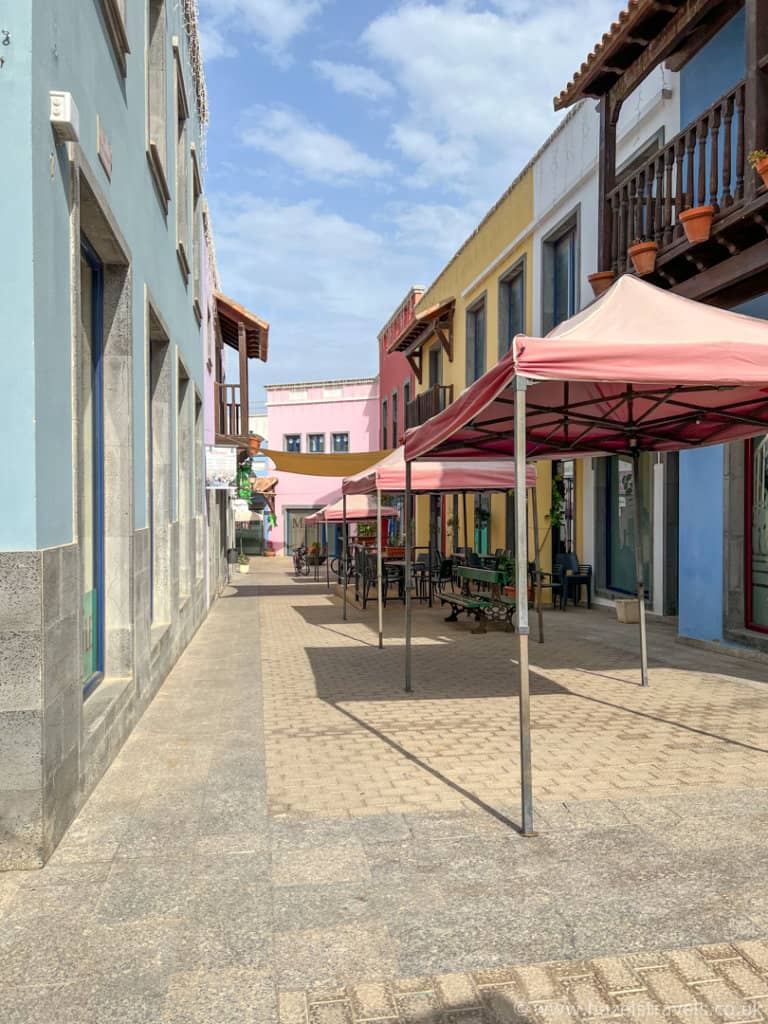 A Spanish street with coloured buildings and empty red canopies ready for an outdoor market.