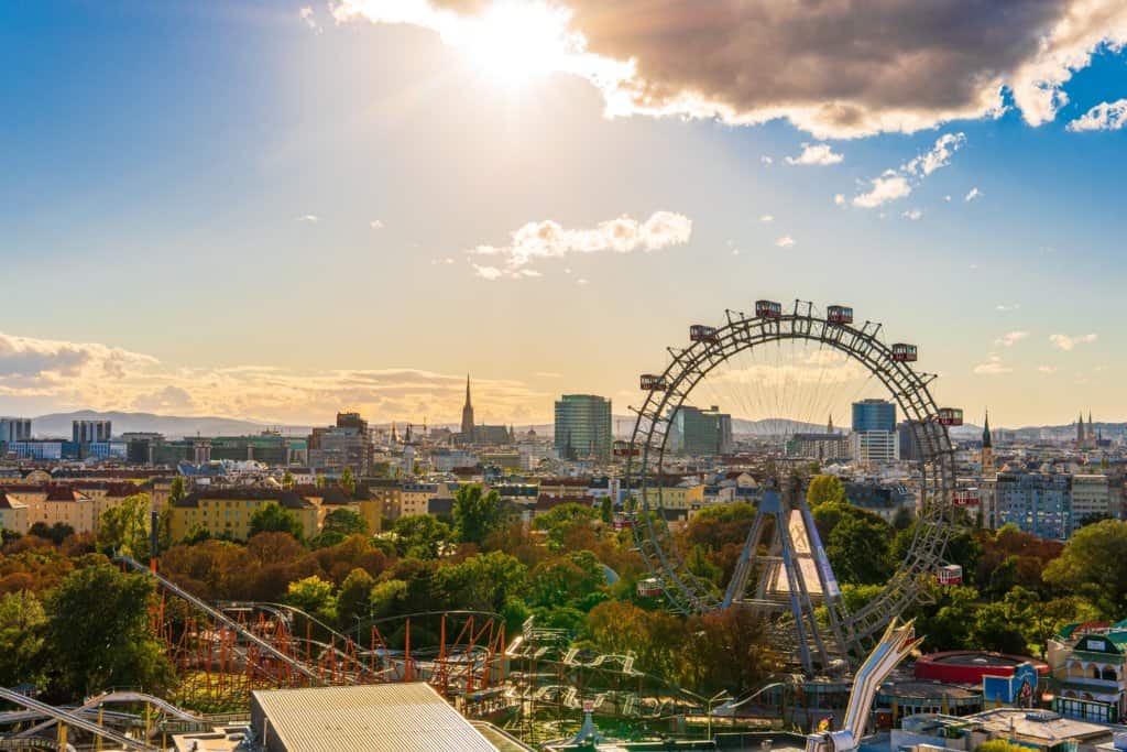 Early evening golden hour landscape shot of Vienna skyline, with a ferris wheel dominating the image onthe right. Fall colours in the foliage and golden hues in the sky.