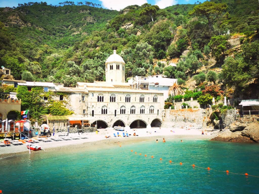 Abbey of San Fruttuoso on the Ligurian coast of Italy — a historic stone monastery with arched windows and a dome, nestled between forested hills and a turquoise cove.