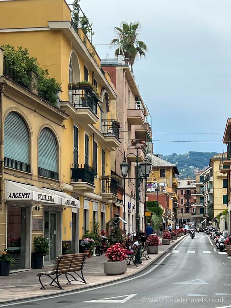 Charming street scene in Santa Margherita Ligure with yellow-painted buildings, balconies, potted flowers, and distant hillside views.