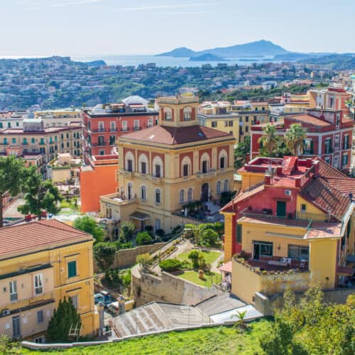 Colorful buildings on a hillside overlooking the sea, with distant islands visible on the horizon.
