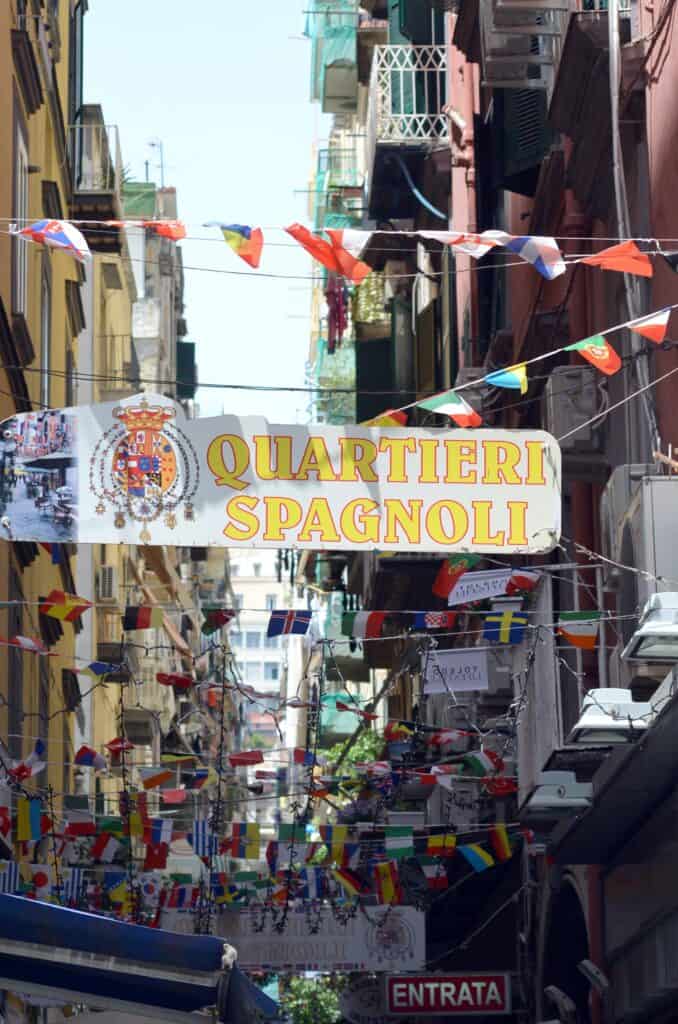 Street in the Quartieri Spagnoli area, with colorful flags and banners hanging between buildings, creating a lively atmosphere.