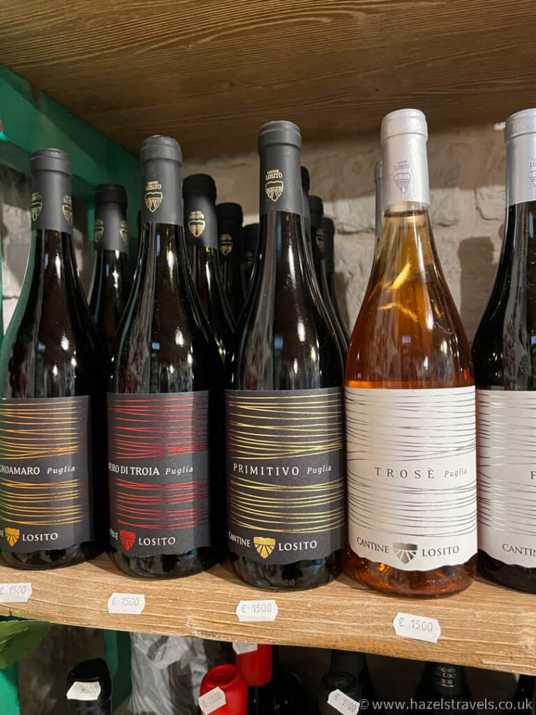 Bottles of Italian wine displayed on a shelf, featuring Alberobello's own Primitivo and Trose varieties, all with visible price tags.