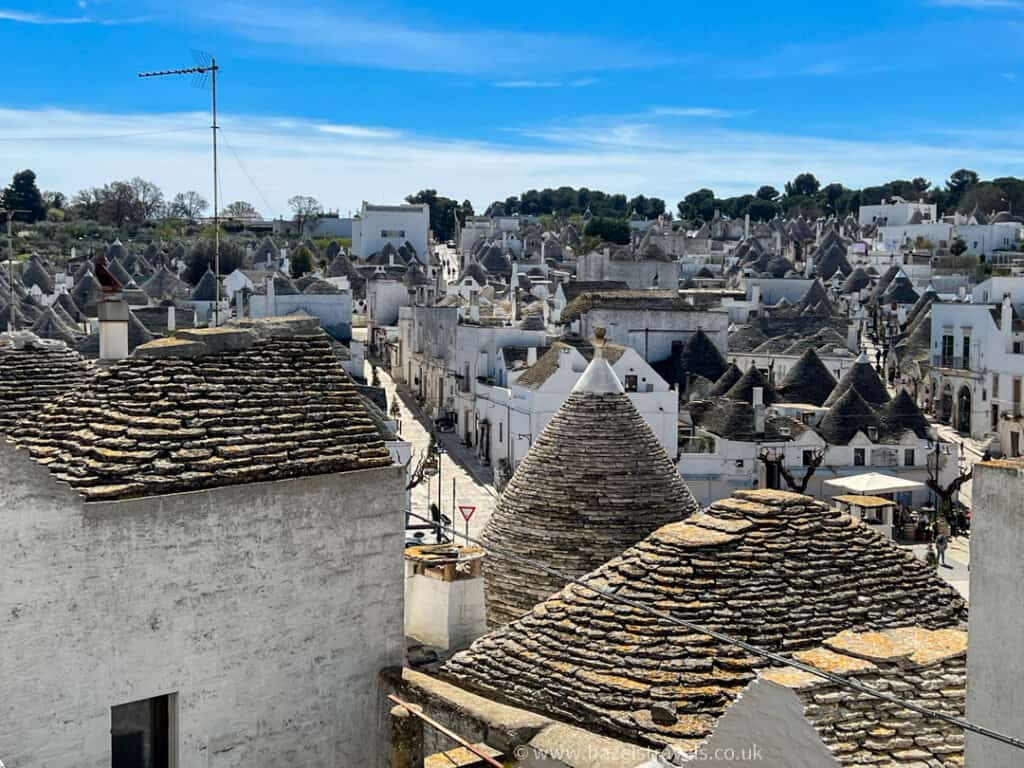 Aerial view of the charming village of Alberobello, showcasing its distinct conical-roofed houses under a bright blue sky.