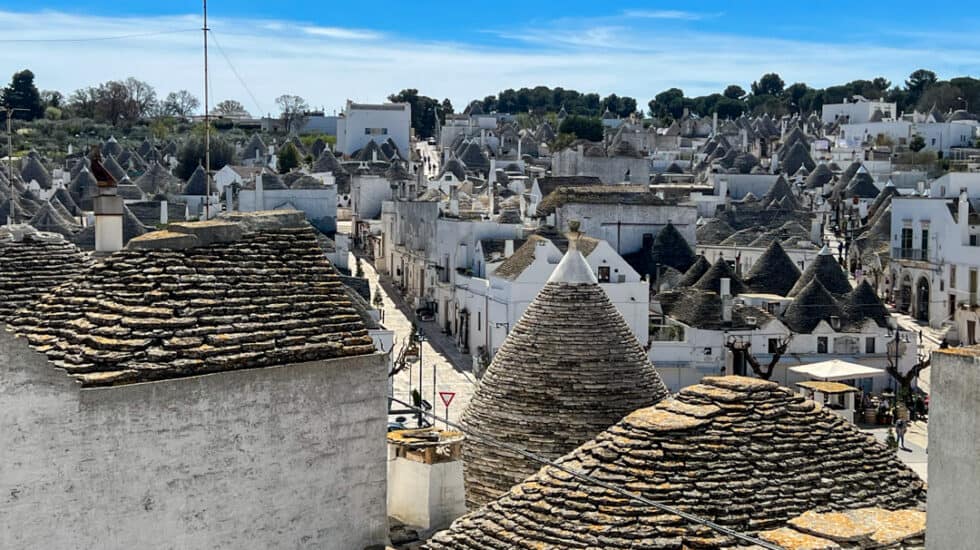 Aerial view of the charming village of Alberobello, showcasing its distinct conical-roofed houses under a bright blue sky.