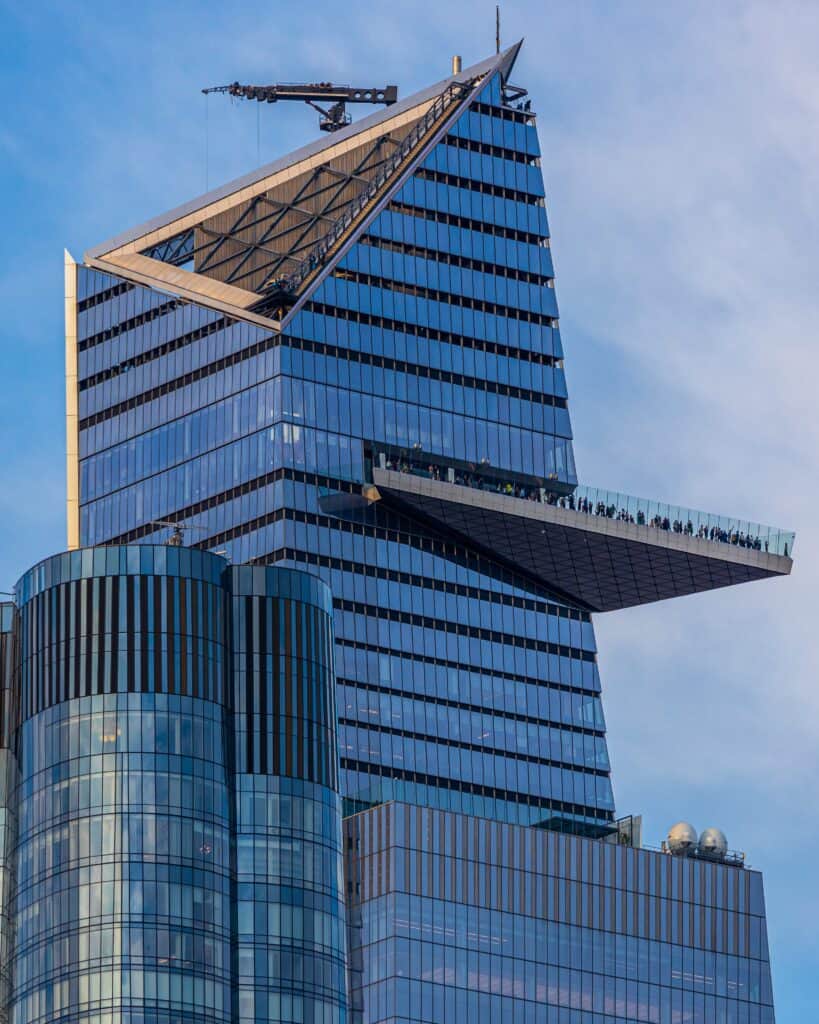 A modern skyscraper with an angled roof hosts The Edge Platform, an external observation deck where a group of people marvels at the city view.