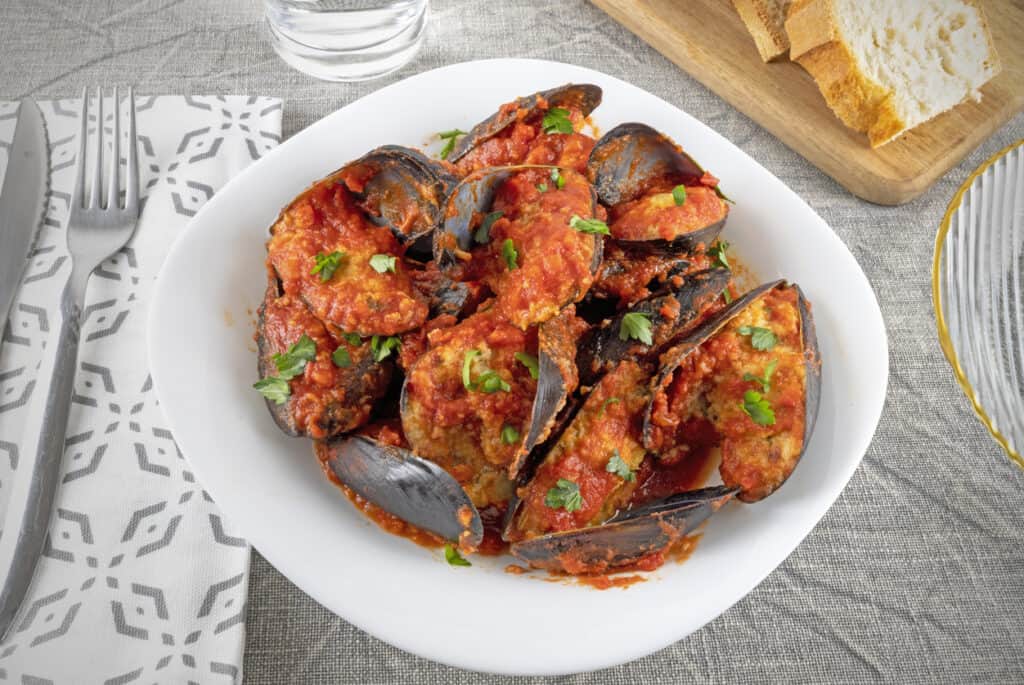 a white plate topped with mussels covered in sauce.