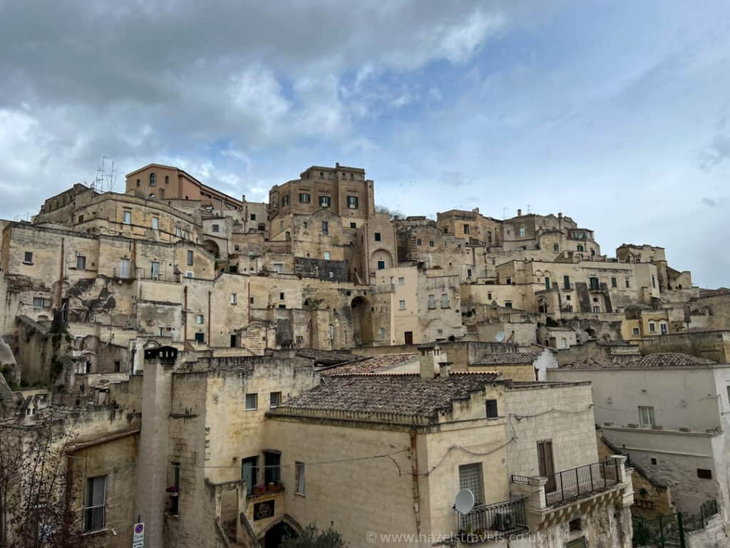 Stone buildings with weathered facades are stacked on a hillside under a cloudy sky.
