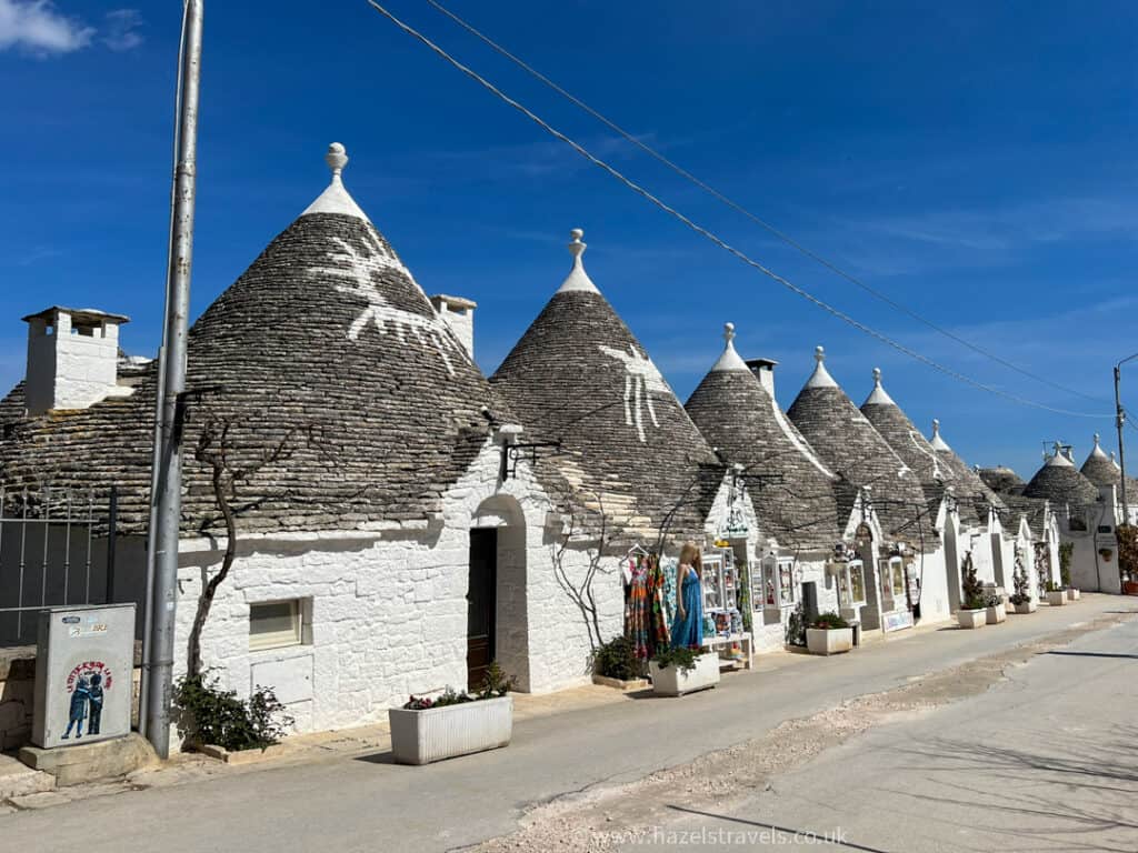 Row of traditional white Trulli houses with conical roofs under a clear blue sky.