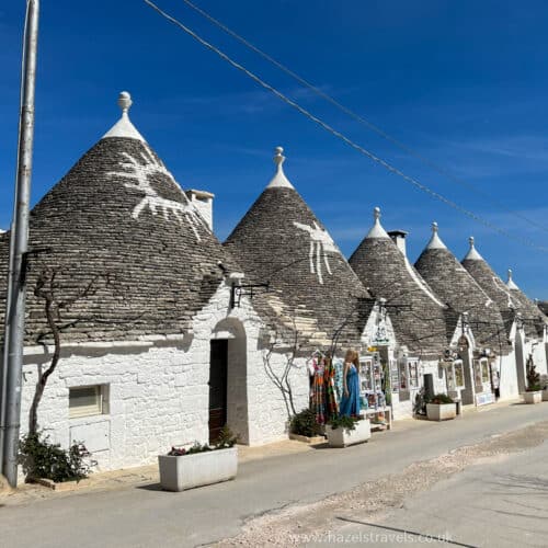 Row of traditional white Trulli houses with conical roofs under a clear blue sky.