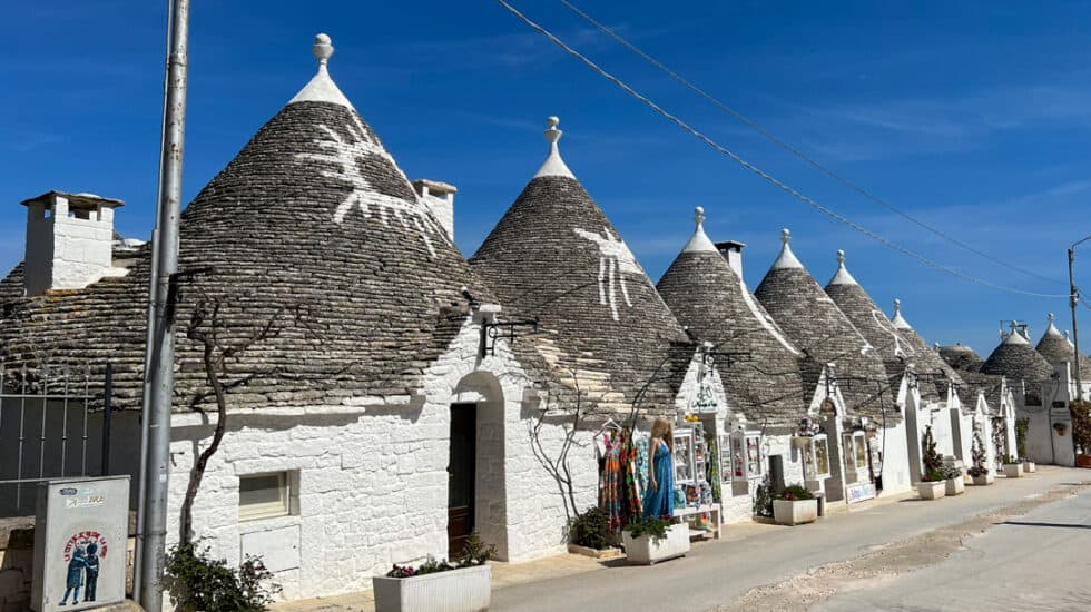 Row of traditional white Trulli houses with conical roofs under a clear blue sky.