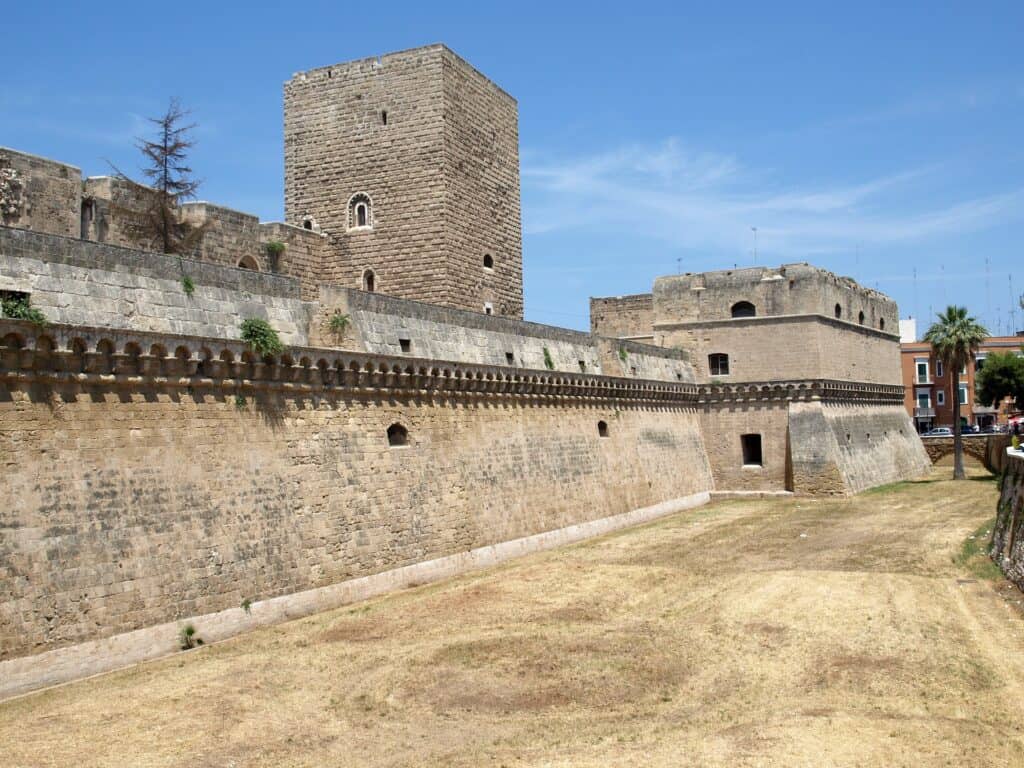 A stone fortress with high walls and a central tower under a clear blue sky. The dry grass surrounds the fort's base.