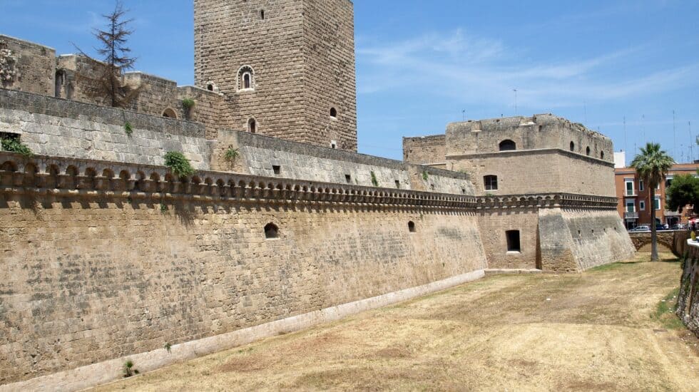 A stone fortress with high walls and a central tower under a clear blue sky. The dry grass surrounds the fort's base.