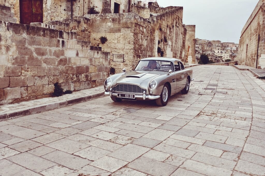Classic silver car parked on a cobblestone street next to old stone buildings.