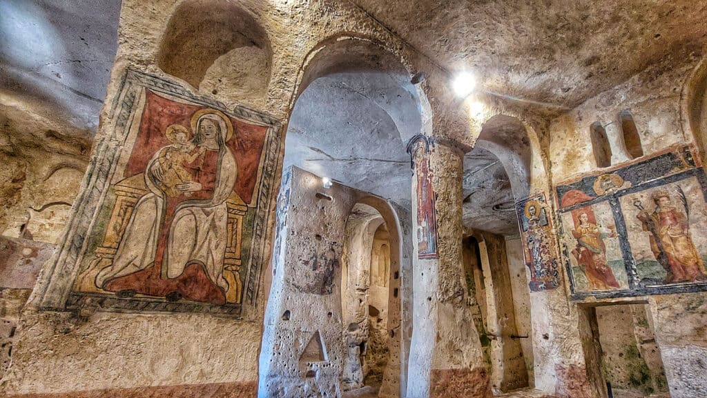 Ancient stone room with arched ceilings and religious frescoes on the walls, depicting figures and scenes.