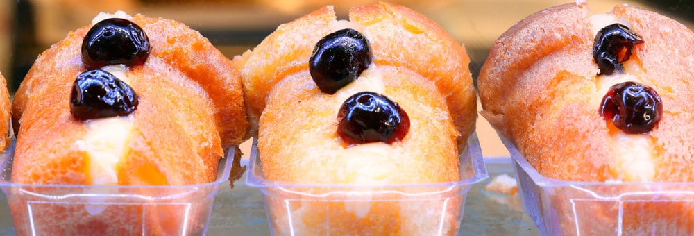A close-up of three delicious pastries, reminiscent of the famed baba from Naples, Italy, filled with luscious cream and topped with dark cherries in clear containers.