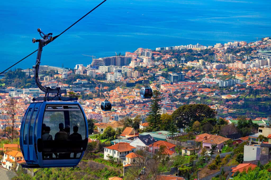 Funchal cable cars transport people over a hillside cityscape, offering breathtaking views of the ocean in the background.
