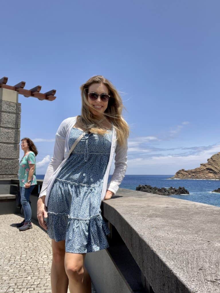 A woman in a blue dress leaning against a wall near the ocean at Porto Moniz Madeira.