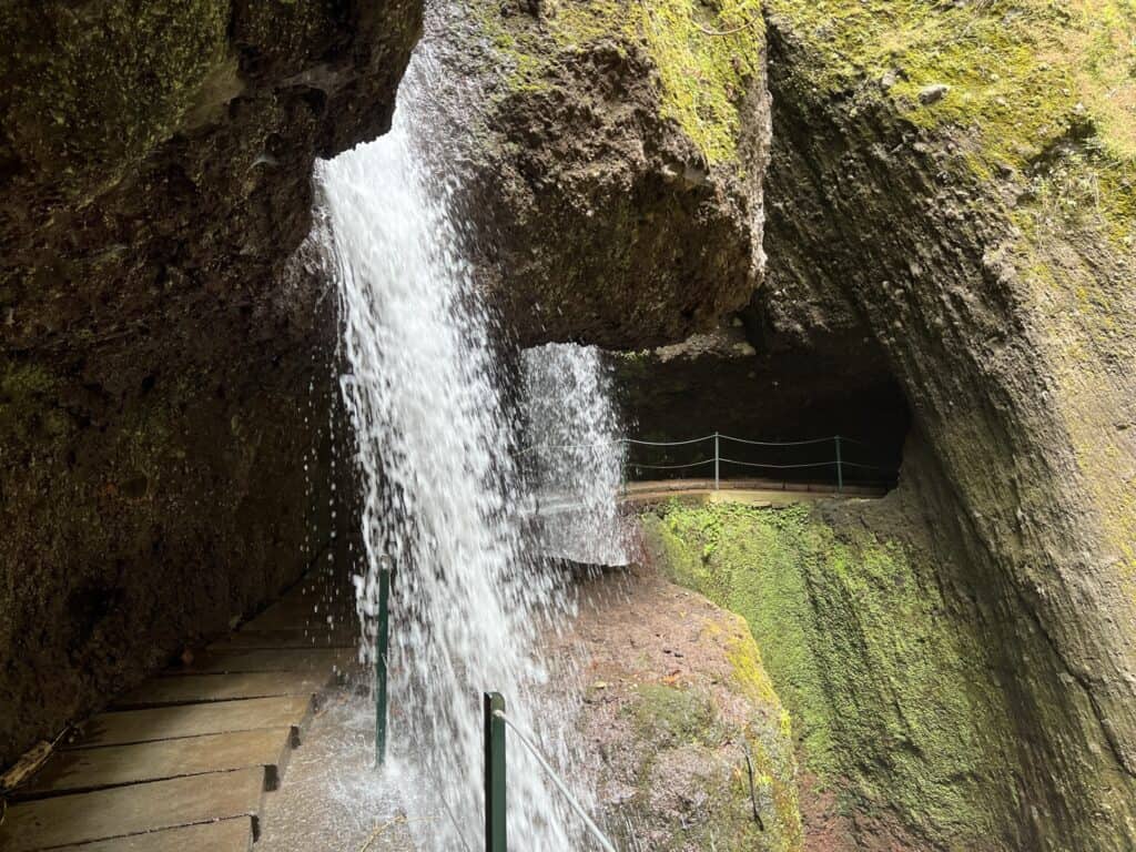 A waterfall in a rocky area with stairs leading up to it on a levada walk in Madeira.