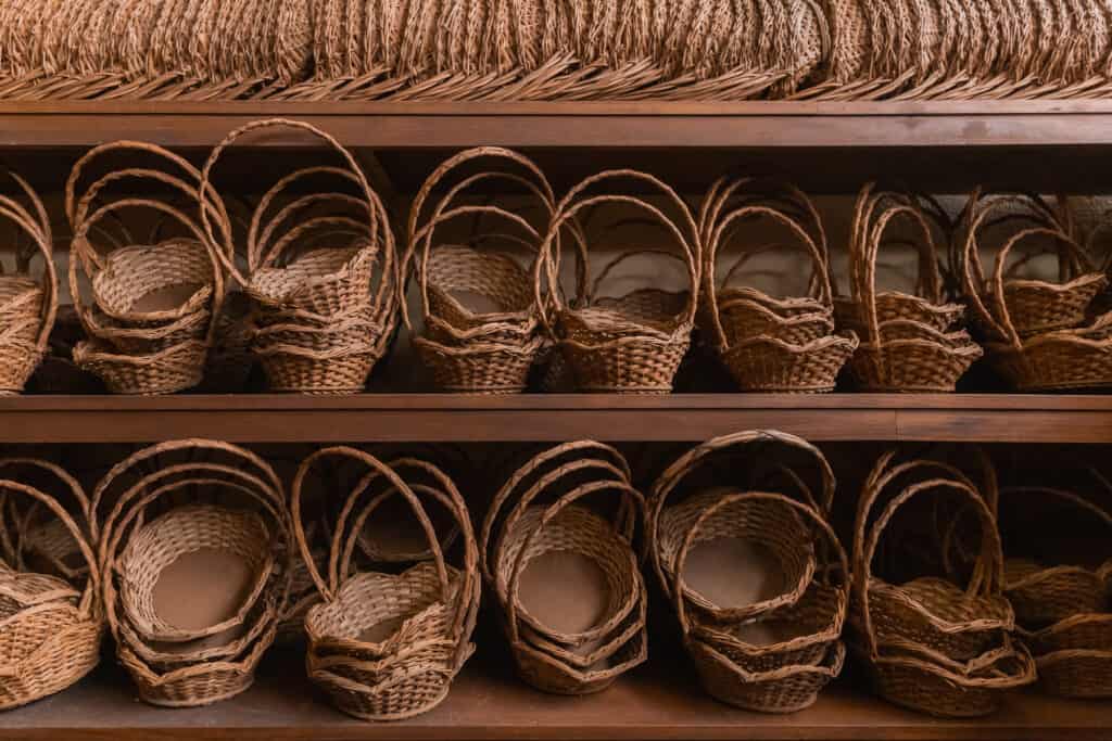 Wooden shelves displaying a variety of empty wicker baskets with handles, neatly arranged in rows.