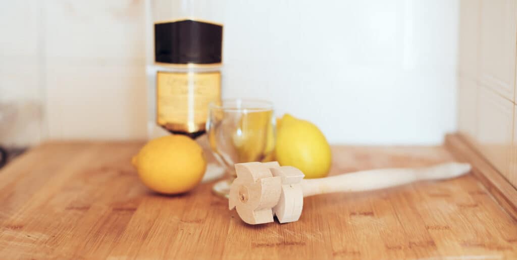 Wooden lemon reamer, two lemons, a bottle, and a glass cup on a wooden surface.