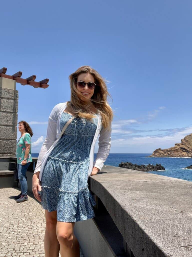 A woman is posing in front of a wall with the ocean in the background in Madeira, Portugal.