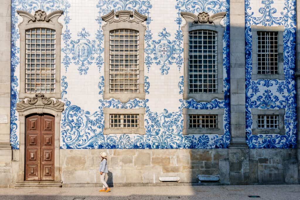 A man is standing in front of a blue and white tiled building in porto.