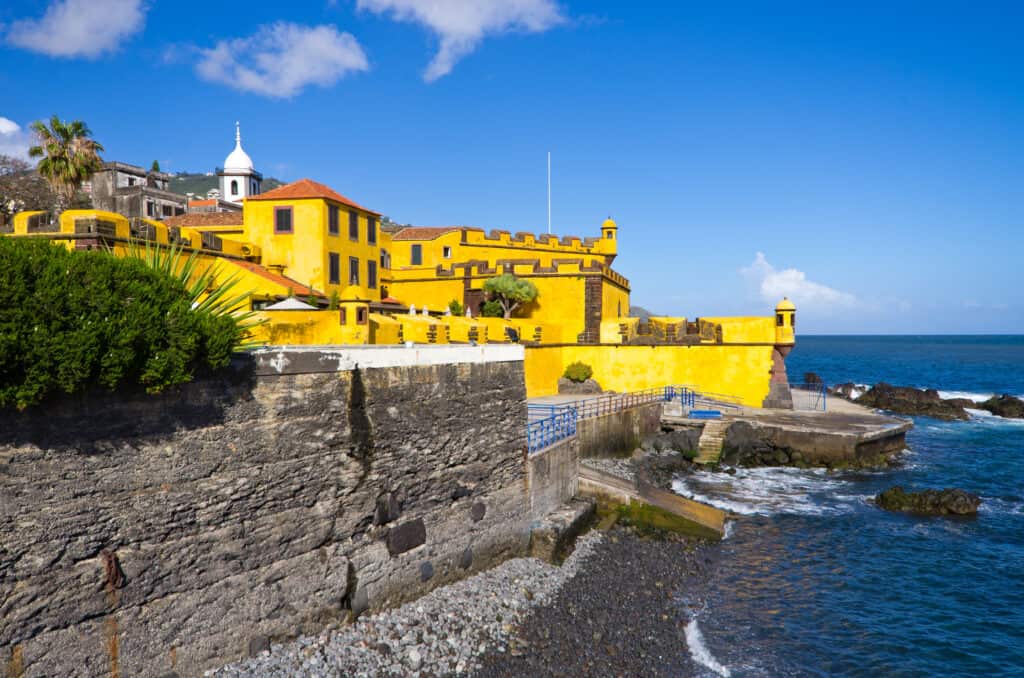 A yellow fort in Funchal Madeira next to the ocean.