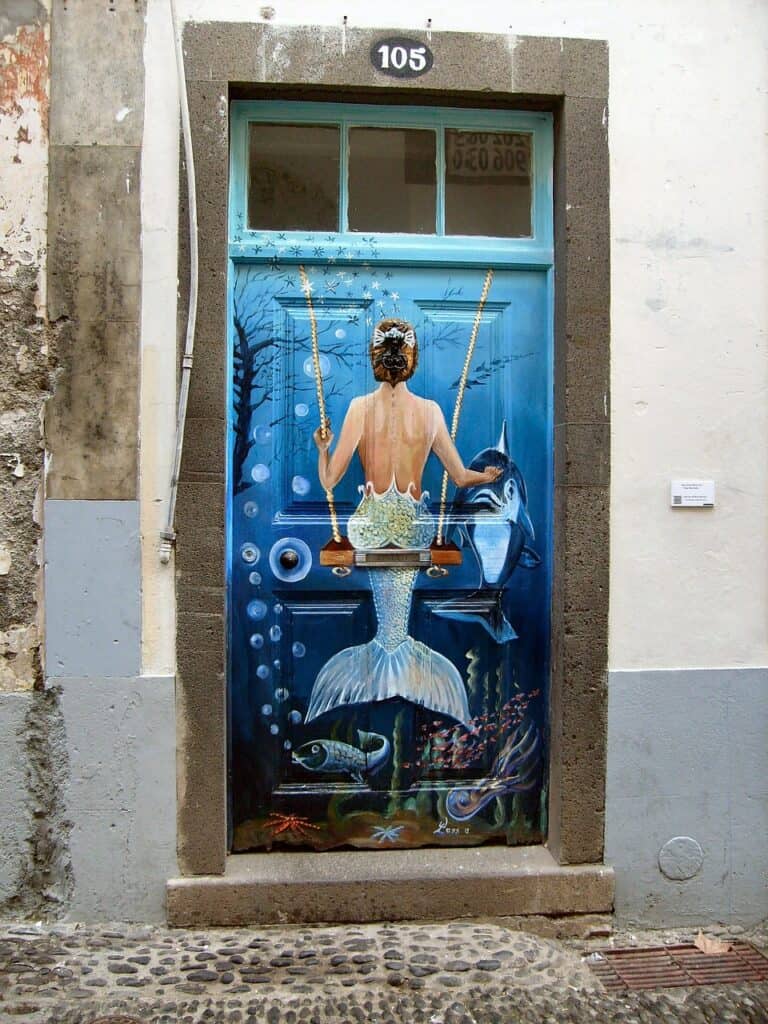 Mermaid mural on a blue door, depicting a mermaid on a swing with marine life around her. Door number 105.