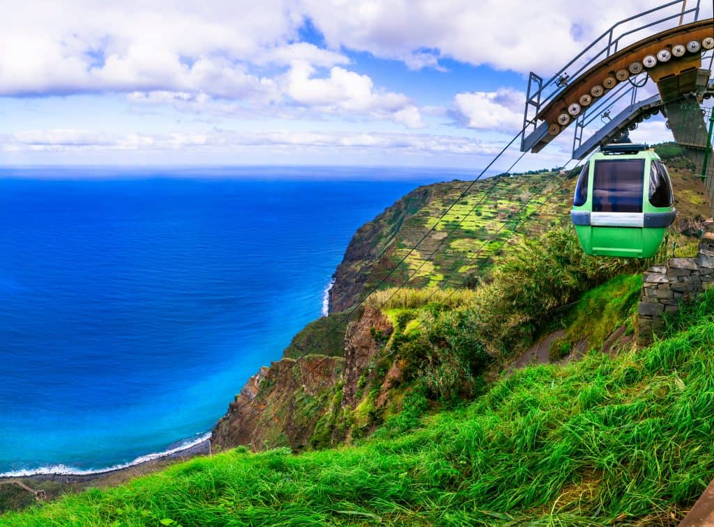 Cable car descending a lush green hillside with a panoramic view of the ocean.