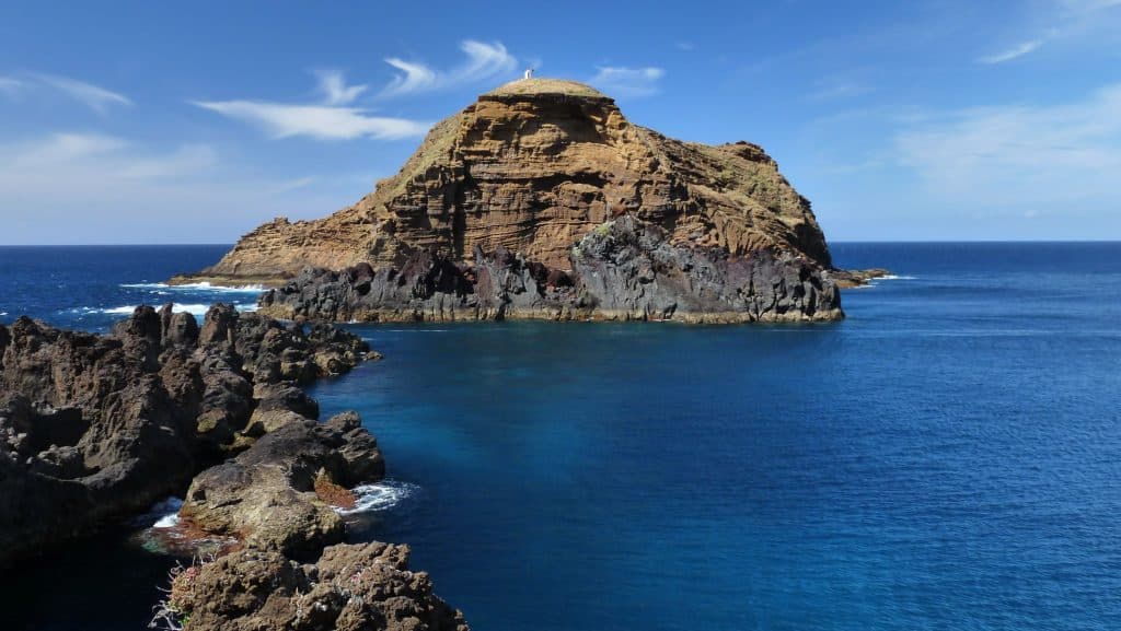 A rocky islet with stratified geologic formations in the azure ocean under a clear blue sky. Porto Moniz Madeira.