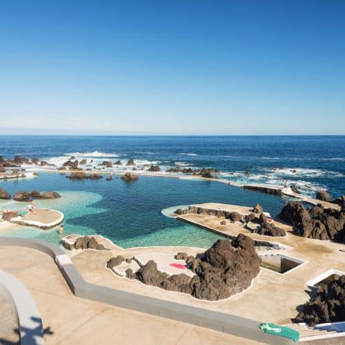 Natural ocean pools In Porto Moniz Madeira, with people enjoying the water on a sunny day.