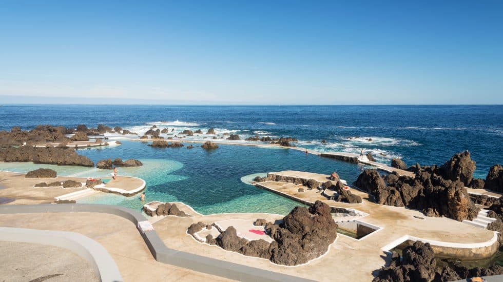 Natural ocean pools In Porto Moniz Madeira, with people enjoying the water on a sunny day.