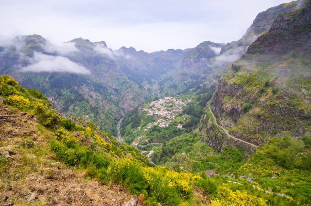 A scenic mountain village shrouded in mist, surrounded by lush greenery and winding roads.