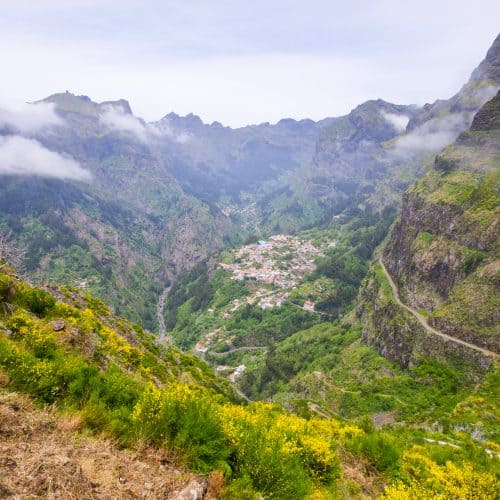 A scenic mountain village shrouded in mist, surrounded by lush greenery and winding roads.