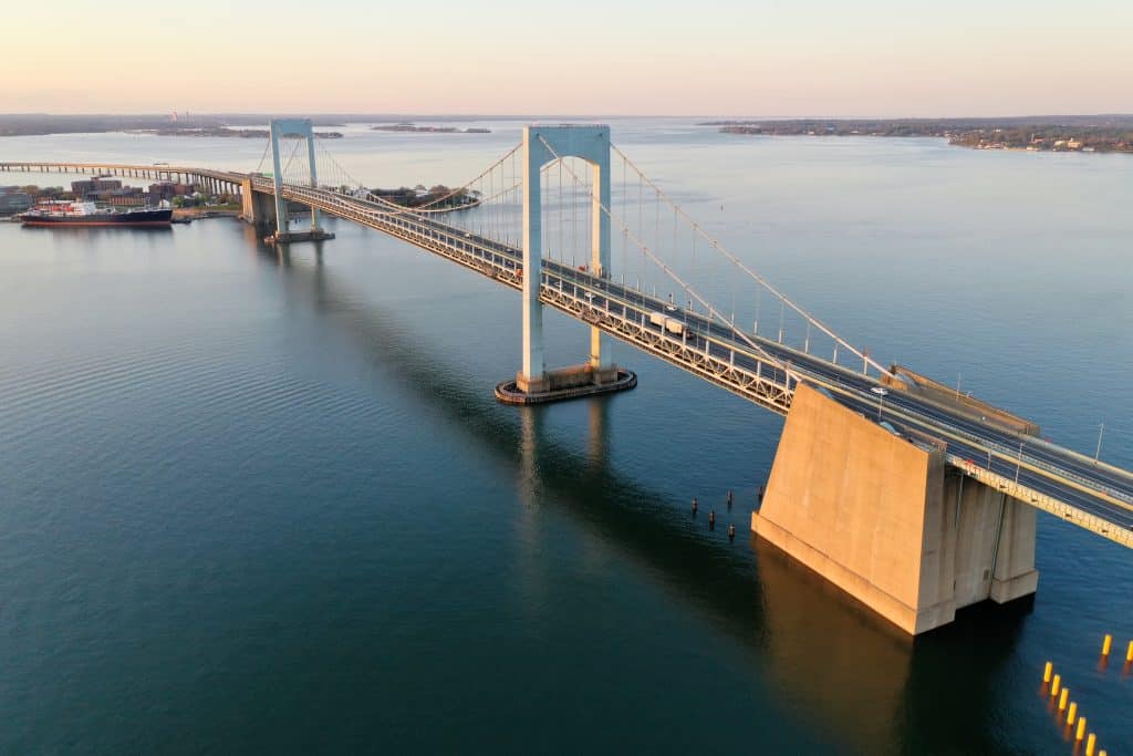 Aerial view of a large suspension bridge spanning a wide river during sunset, with calm waters and clear skies.