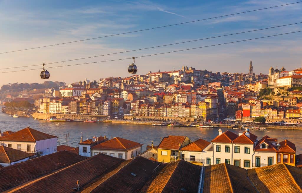 Cable cars over rooftops with a panoramic view of porto, portugal, featuring the douro river and densely packed historic buildings.