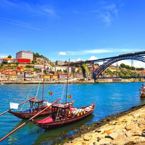 Traditional rabelo boats on the douro river with the dom luis i bridge and the porto skyline in the background, portugal.