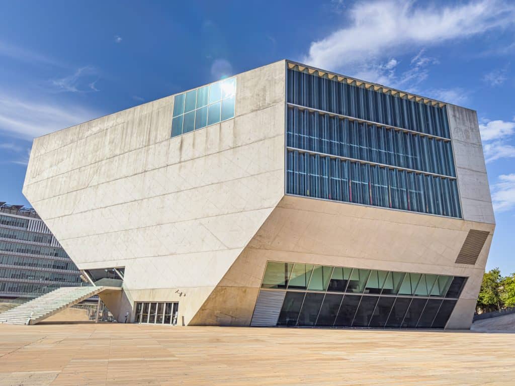 Things to do in Porto - Casa de Musica. Modern geometric building with large windows, a tilted facade, and stairs under a blue sky.