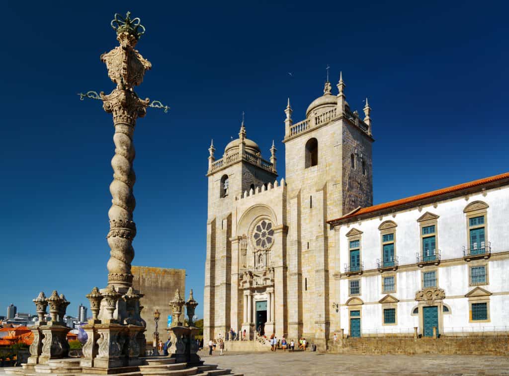 Historic porto cathedral and ornate pillory column under a clear blue sky, with visitors walking around the plaza.